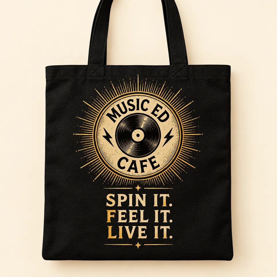Mockup of a black canvas tote bag printed with a gold sunburst Music Ed Cafe badge and the words Spin It. Feel It. Live It.
